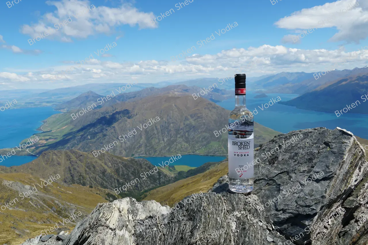 BROKEN SHED VODKA ON OUTCROPPING WITH MOUNTAINS AND LAKES N BACKGROUND