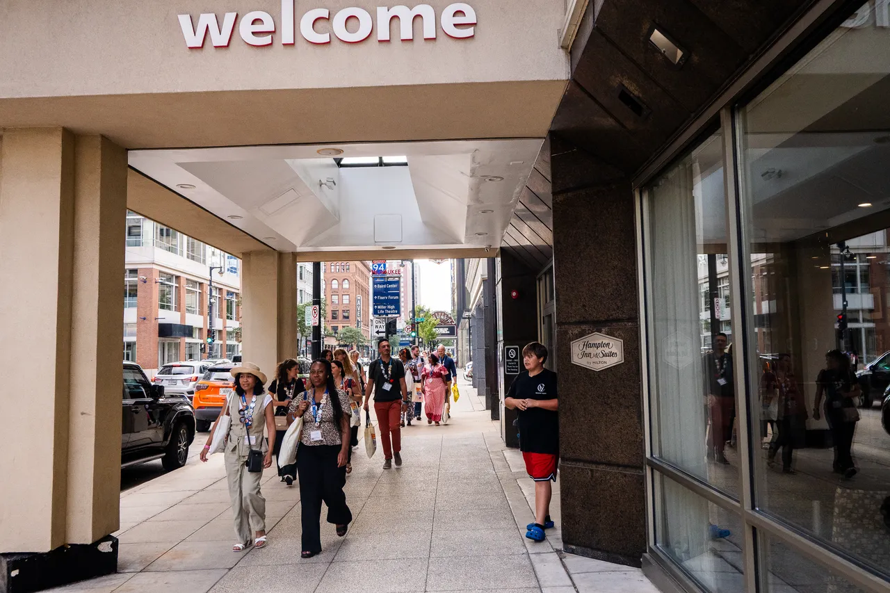 Visitors walk along a covered downtown sidewalk beneath a large welcome sign.
