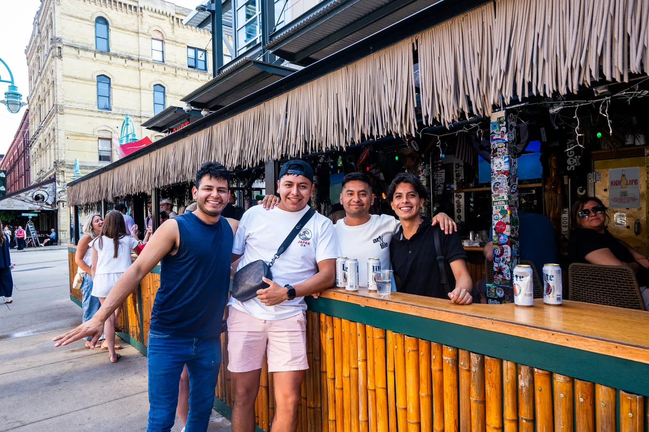 Four friends pose at a bamboo-fronted outdoor bar on a downtown street.