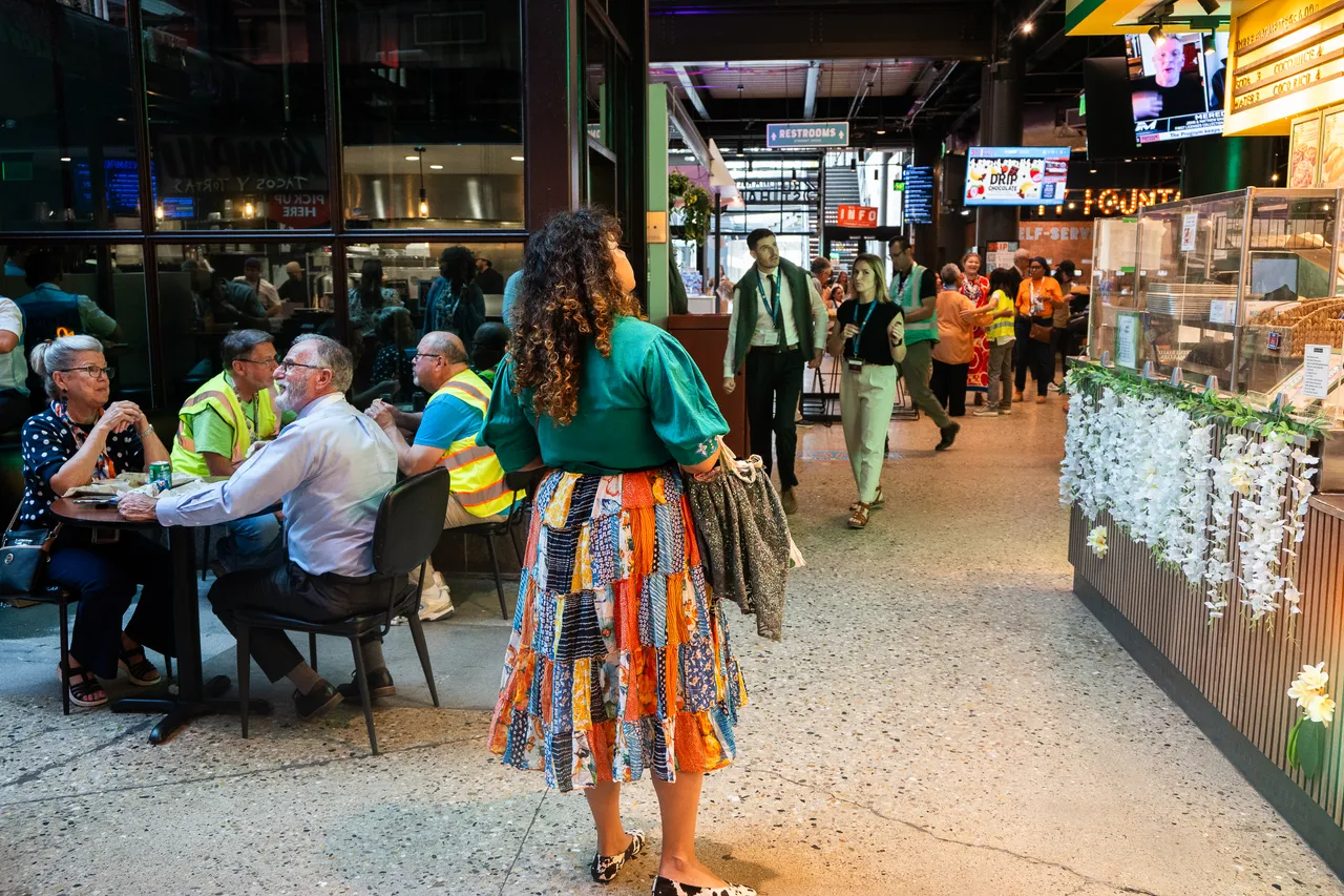 Visitors dine and walk through a busy indoor food market lined with colorful stalls.