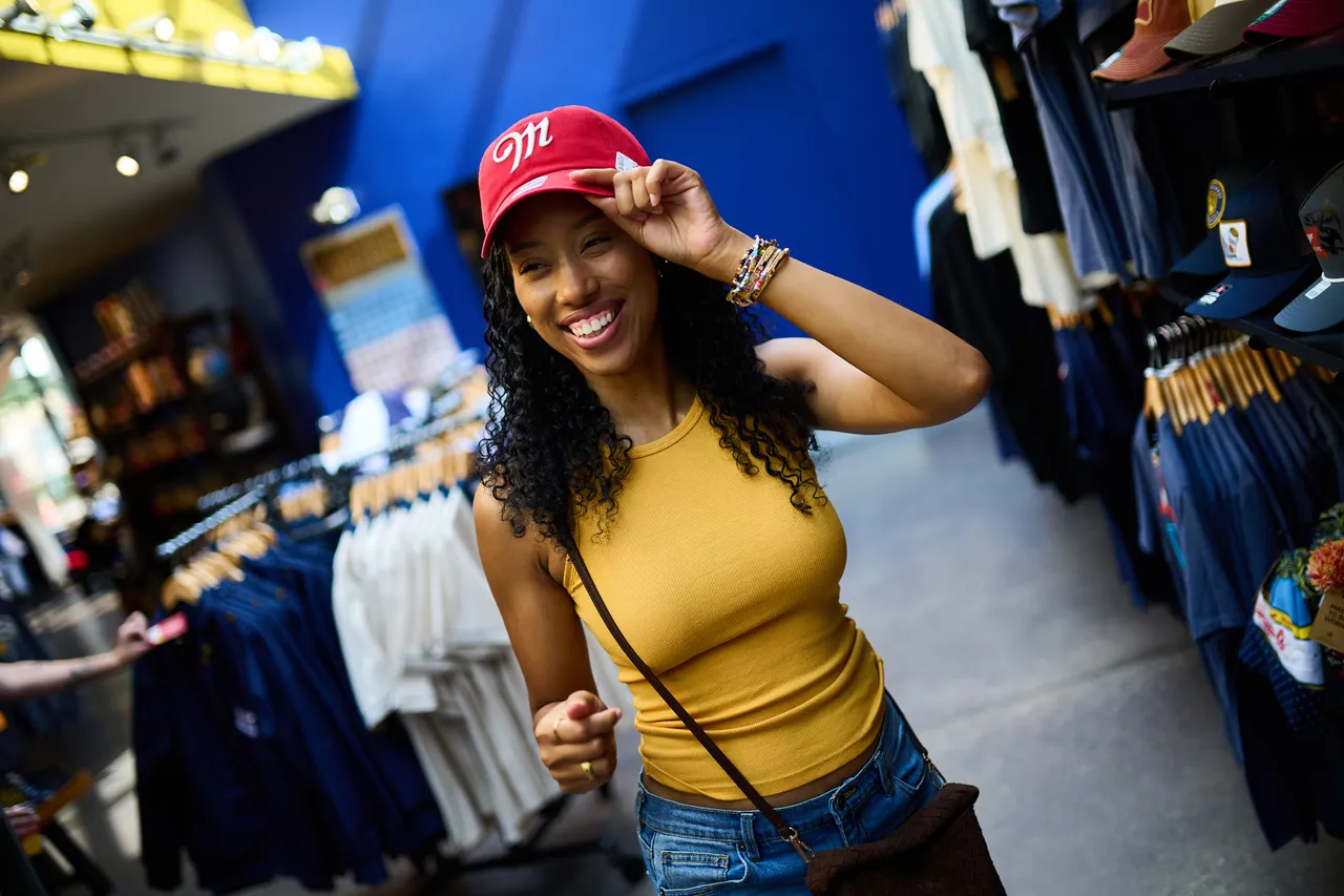 A smiling woman adjusts a red Milwaukee cap in a clothing and souvenir shop.