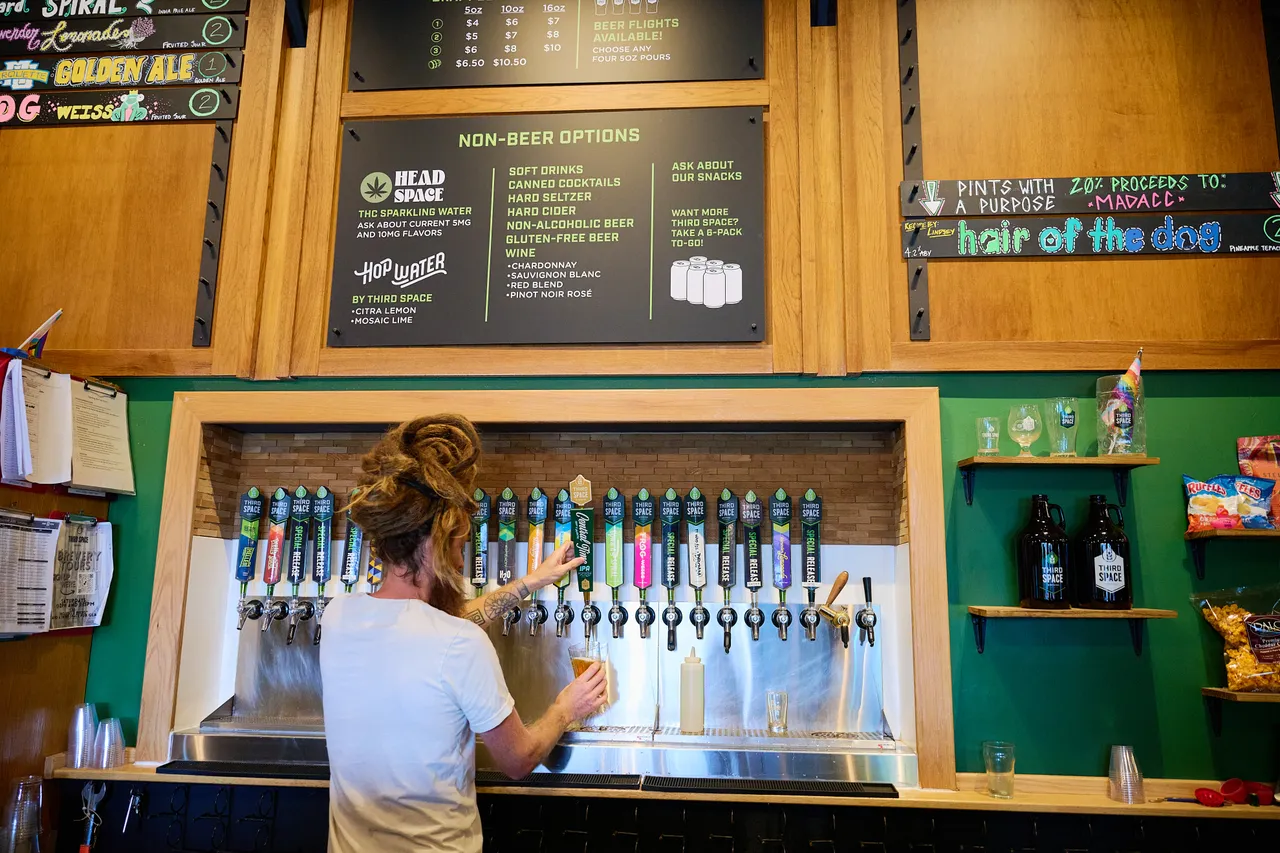 A bartender serves a drink beneath rows of taps at a wood-paneled taproom bar.