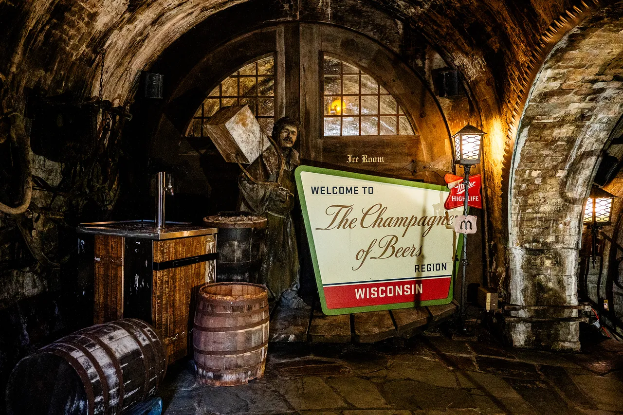 A stone beer cellar display features wooden barrels, a historical figure, and a Wisconsin Champagne of Beers sign.