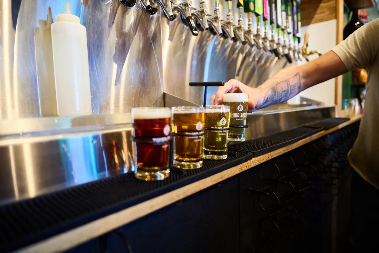 A bartender serves craft beer beside tasting glasses lined up under a row of taps.