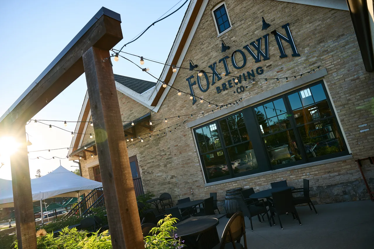 Foxtown Brewing’s stone building and outdoor patio sit beneath string lights in the evening sun.
