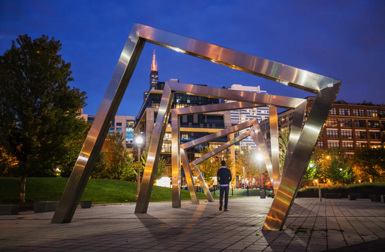 Evening skyline shot of man standing inside sculpture in Bartleme park in the West Loop