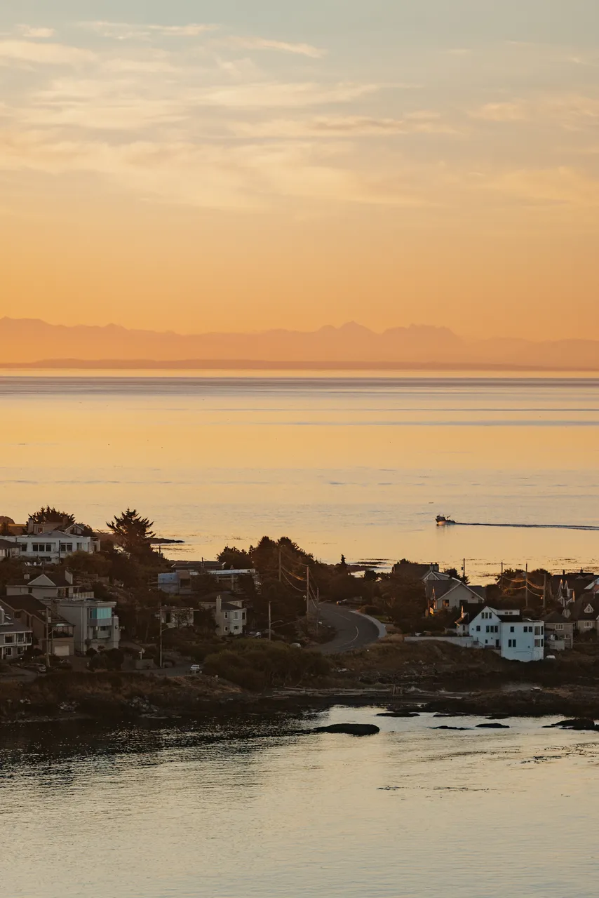 Serene sunset over seaside neighbourhood with mountains in background and orange sky