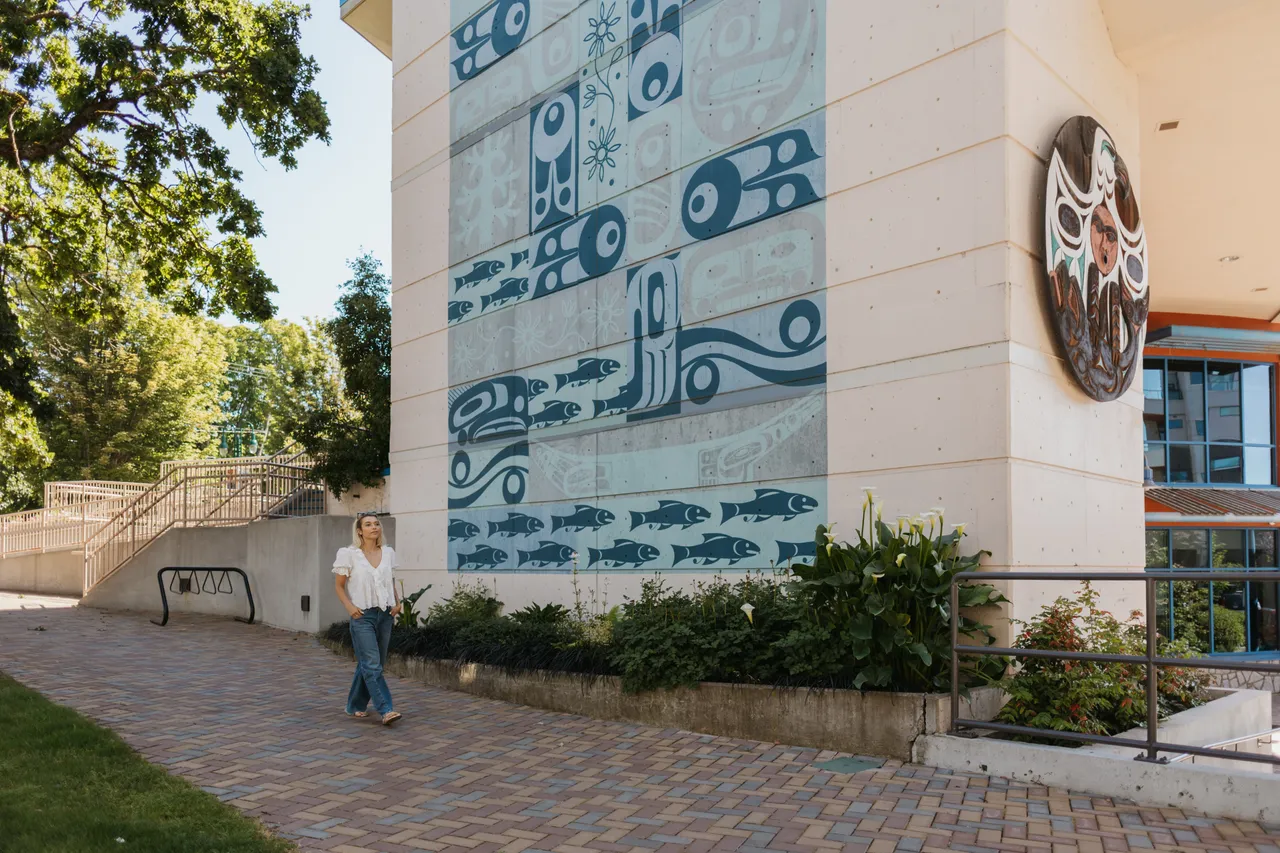Woman Walks in Front of Indigenous Fish Mural on a Sunny Day