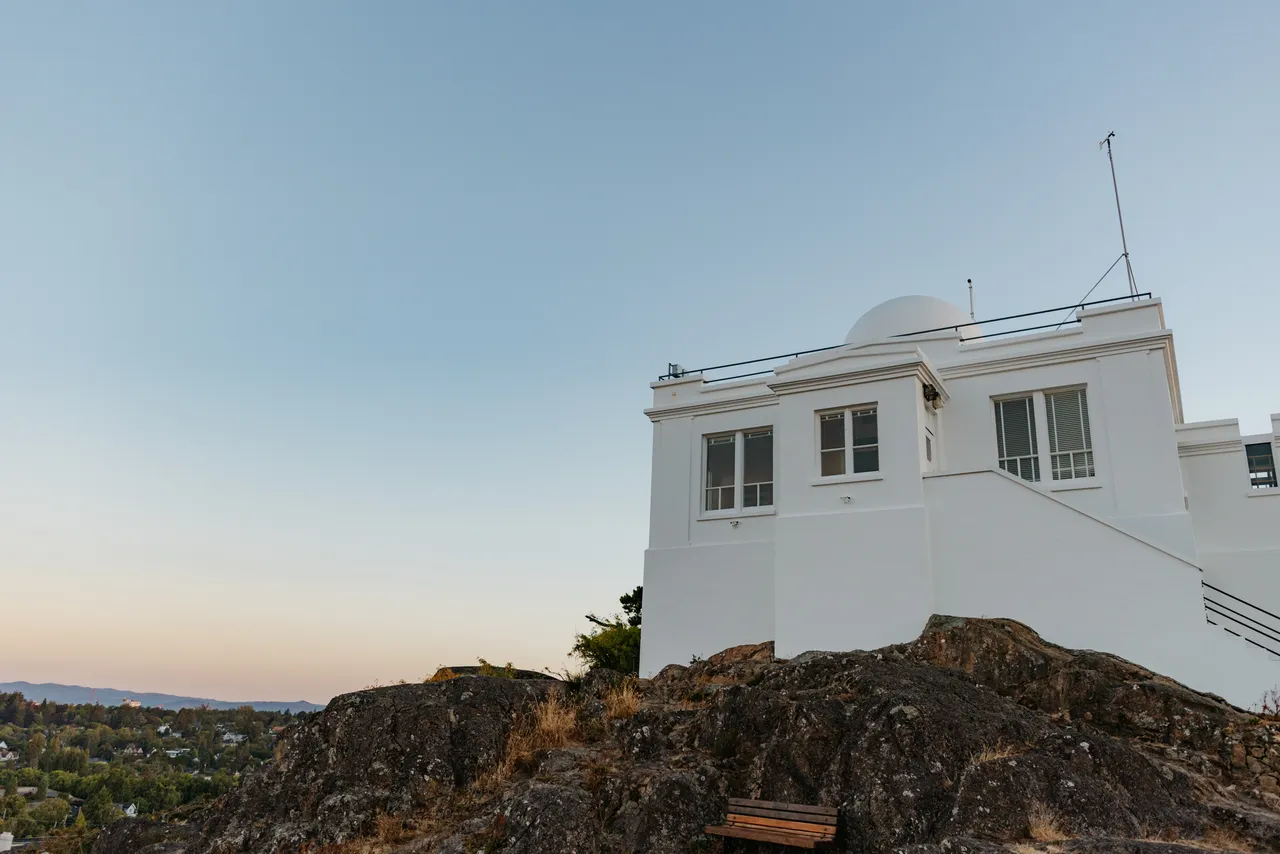 A white building stands on a rocky hill overlooking a town under a clear sky.