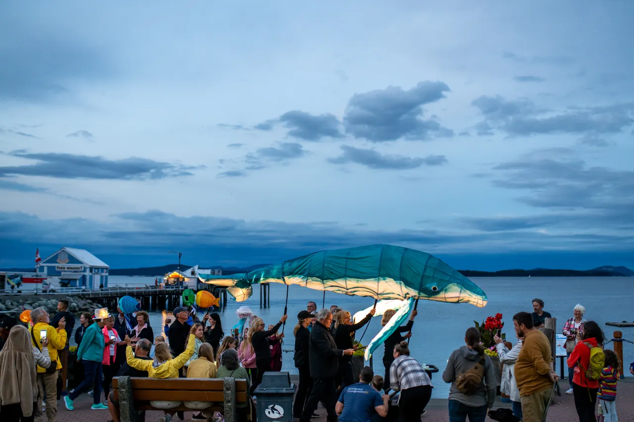 Illuminated Whale Lantern Moves Along Waterfront Past Pier at Dusk