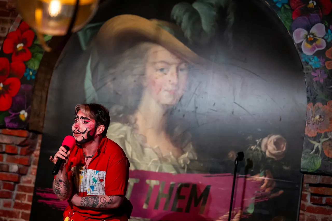 Performer in Front of Let them Eat Cake Painting Talking into Mic