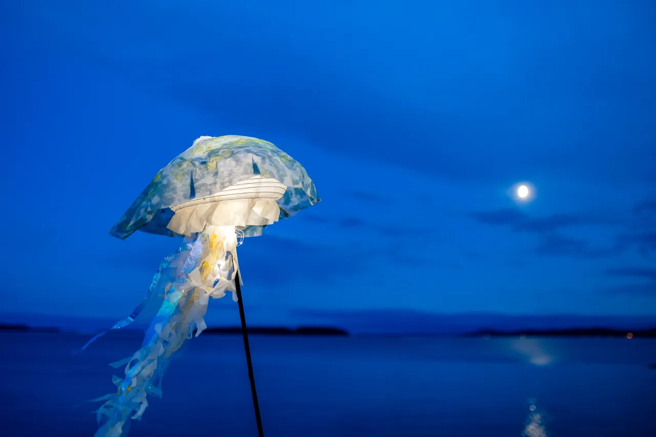 Translucent jellyfish lantern raised against the moon over a still sea