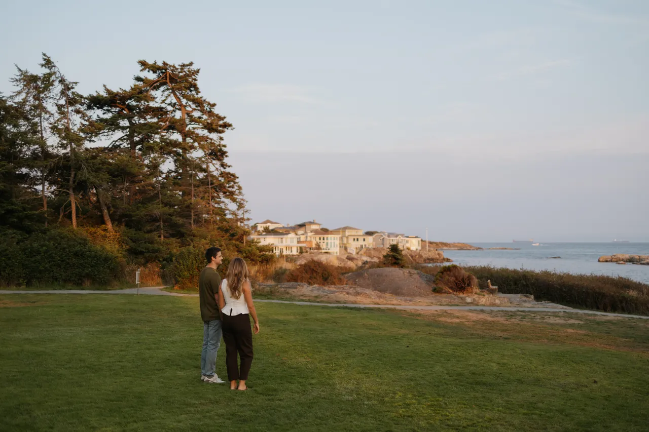 Couple admiring ocean on calm, sunny evening with trees in background