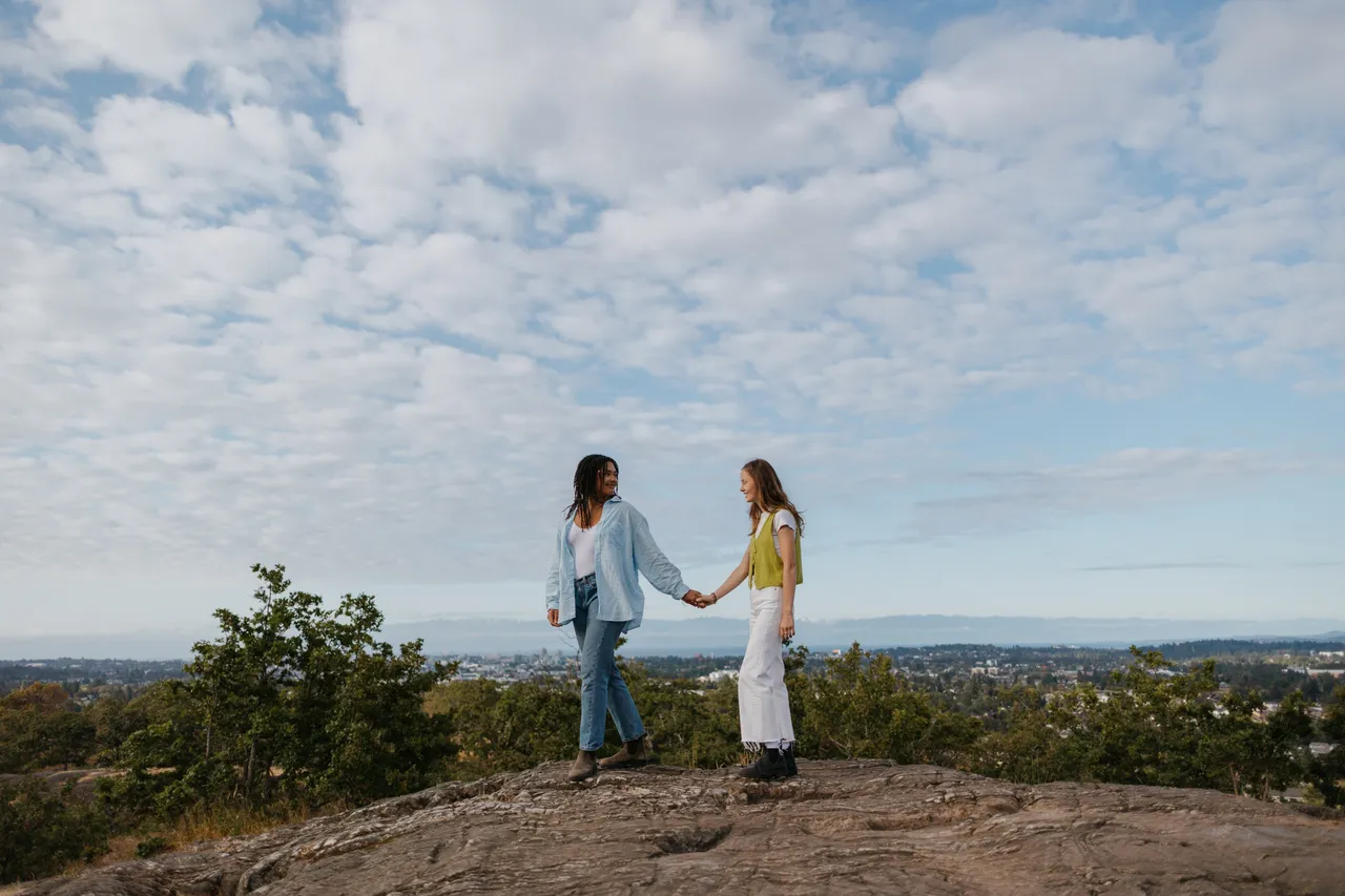 Couple holding hands on rocky hill under bright sky