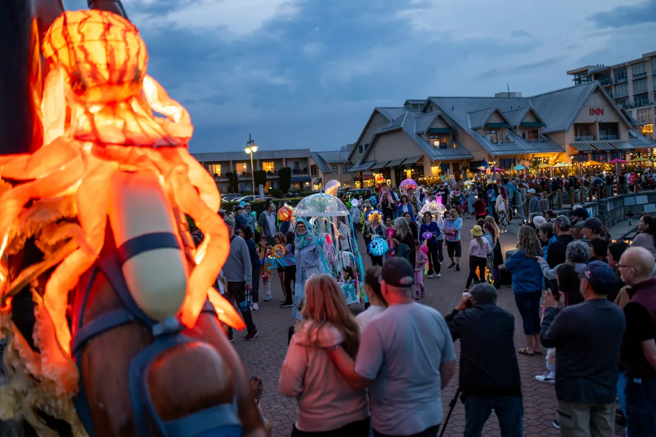 Glowing orange octopus lantern carried through a crowded seaside street at nightfall