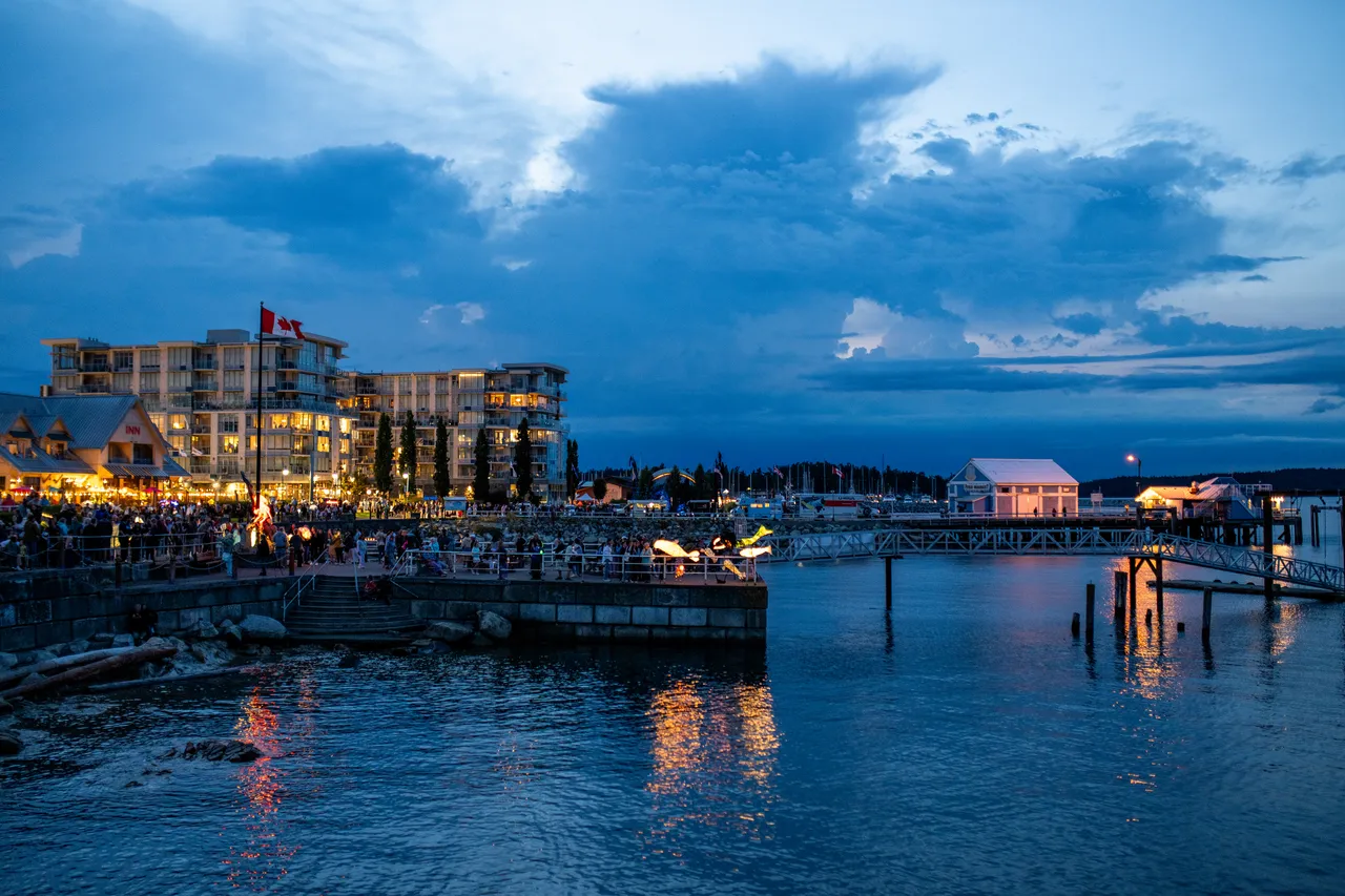 Wide twilight view of a lit waterfront village, docks and reflections