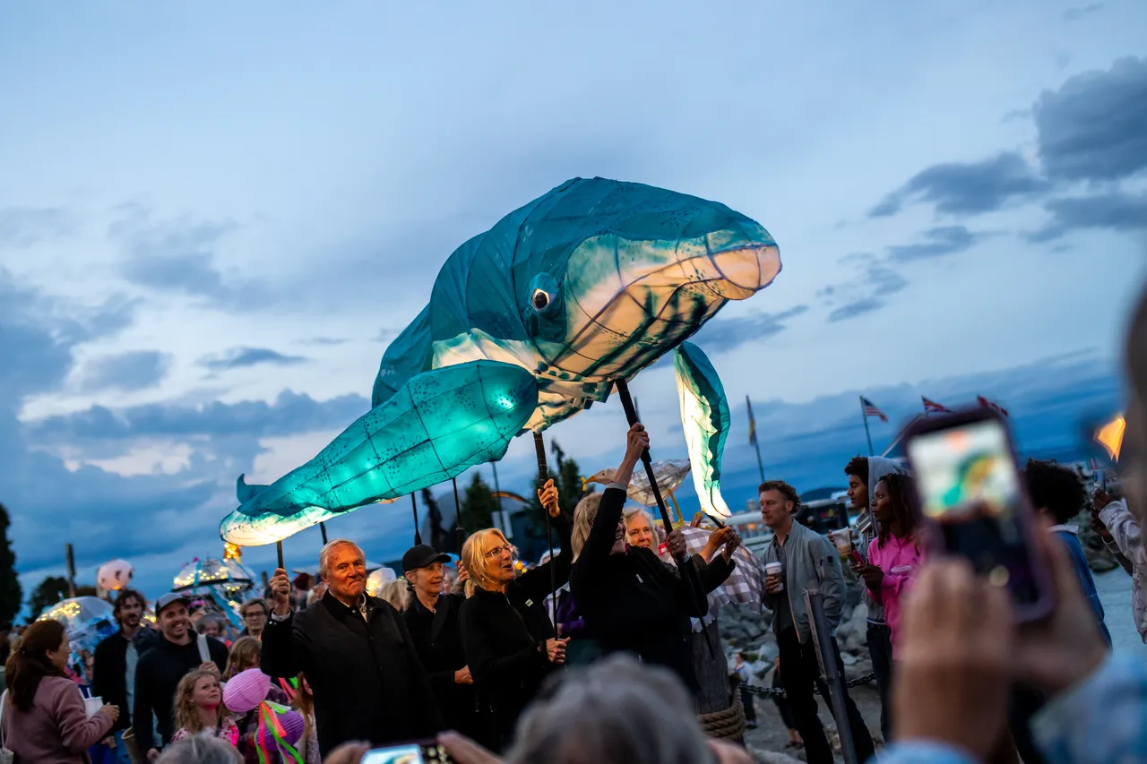 Giant Illuminated Whale Lantern Carried Above Crowd at Waterfront Evening Parade