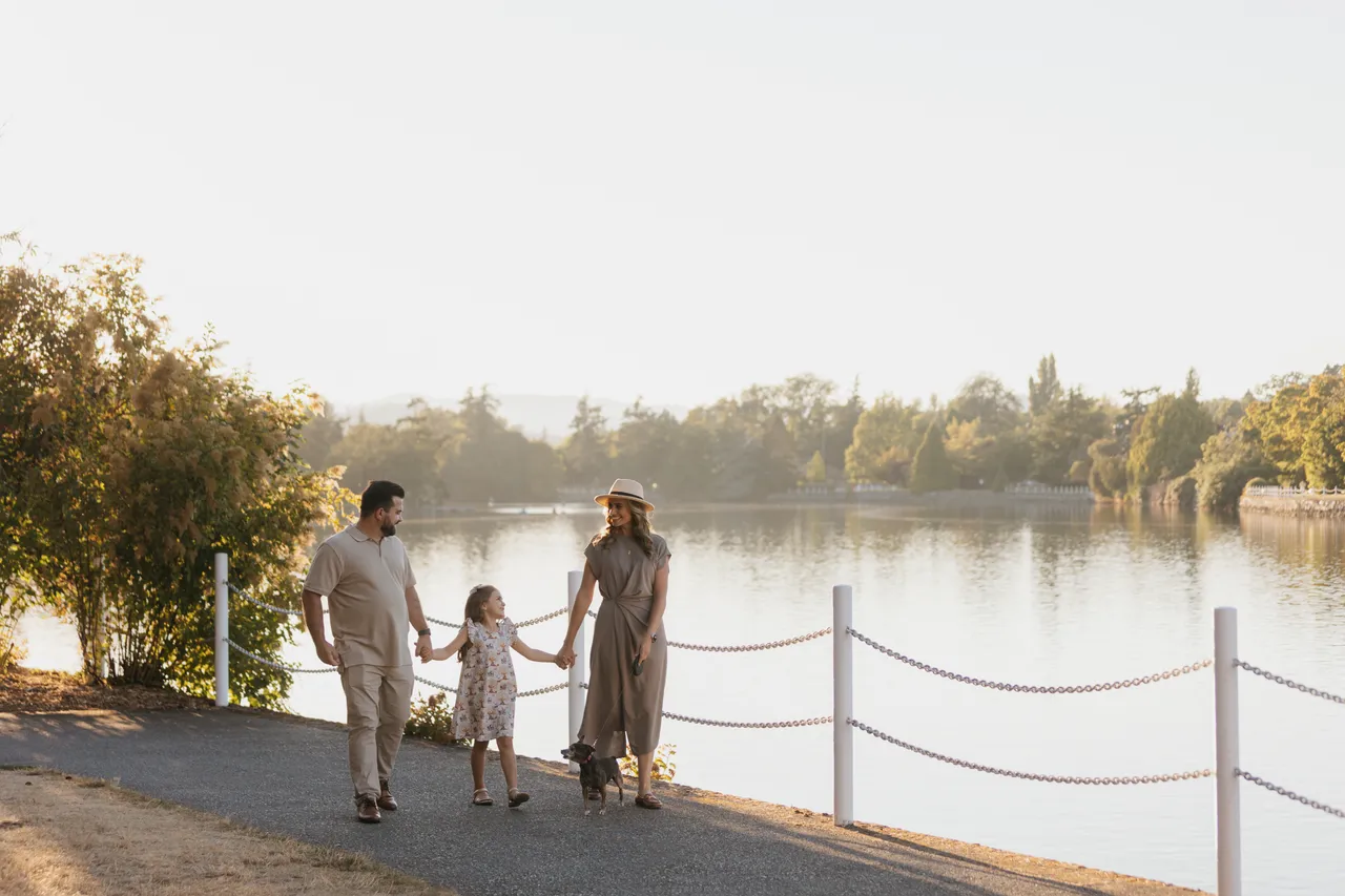 A family walking hand-in-hand along a lakeside pathway with a chain on a sunny day.