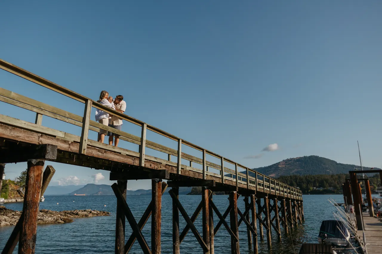Couple standing on a wooden pier over calm water with mountains in background