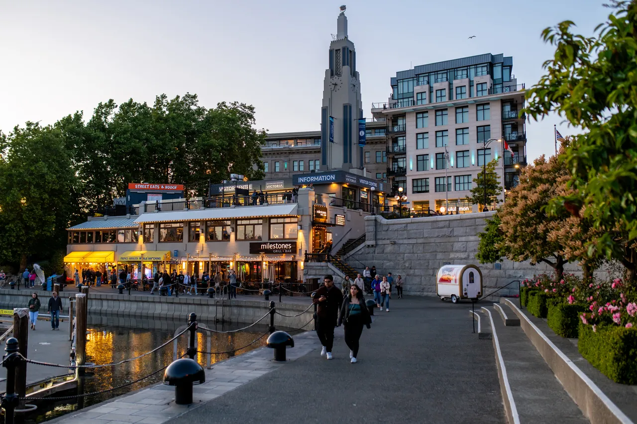 People Walking Along Inner Harbour and Apartments in Background