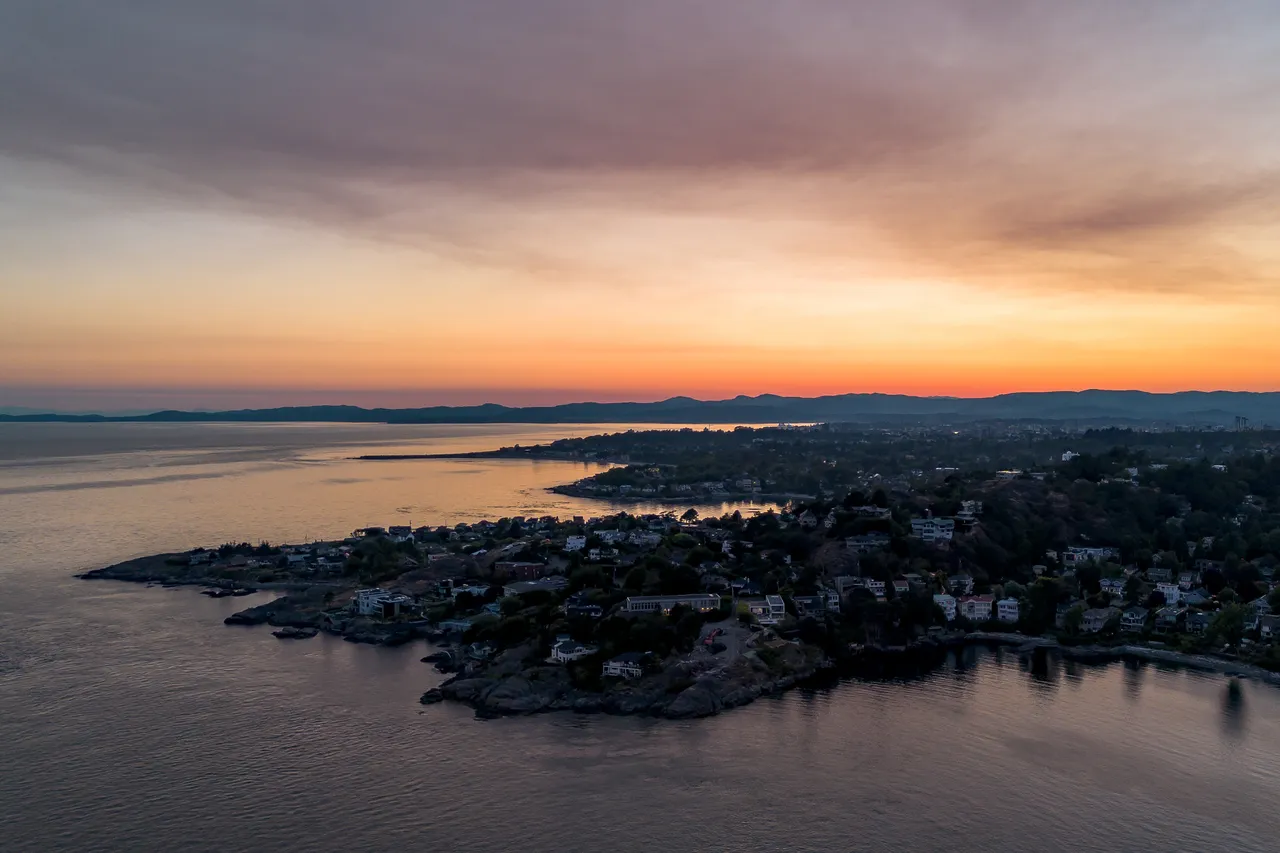 Aerial of Ocean Sunset overlooking Housing with Mountains in Background