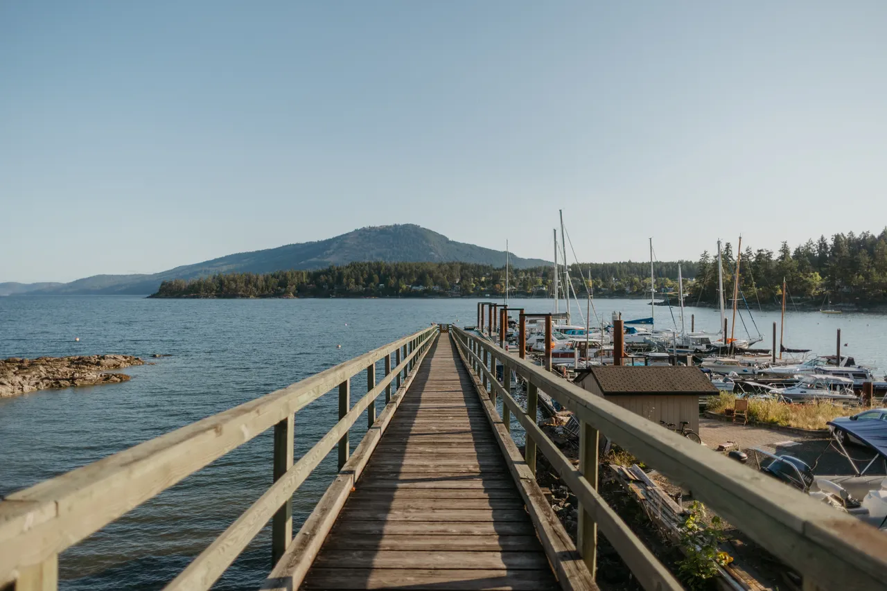 Wooden pier stretching toward calm waters and distant hills with mountains in background near boats