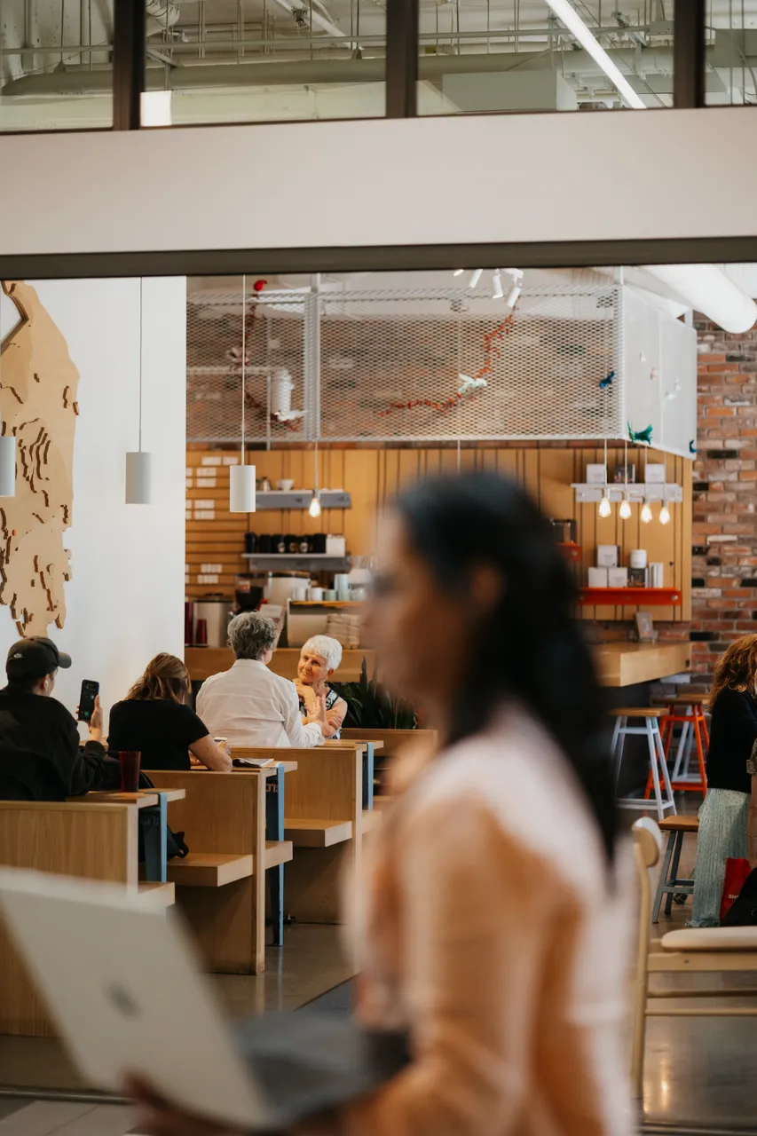 People converse in a cafe while someone sits in the foreground on a bright day