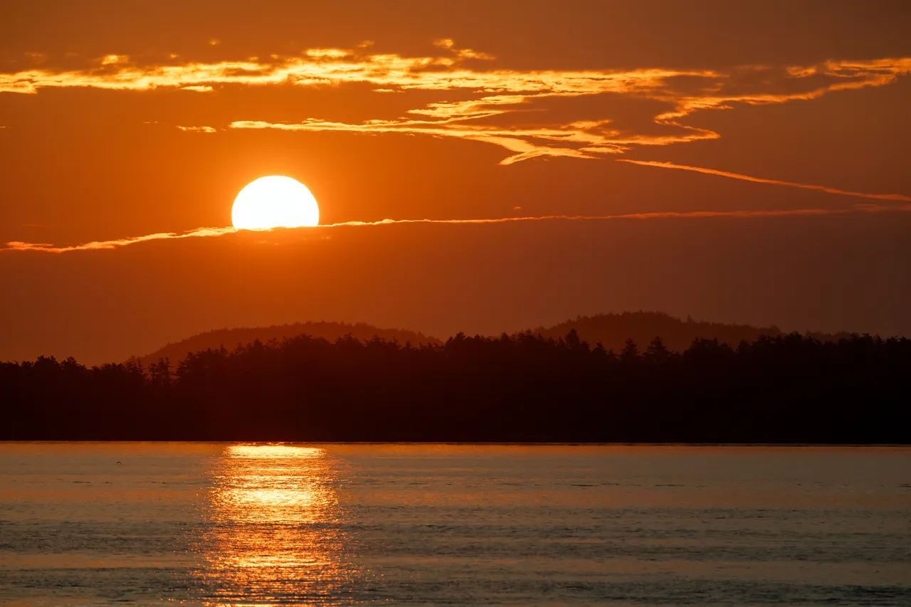 Orange Sun Rises Above Silhouetted Hills Under Streaked Clouds
