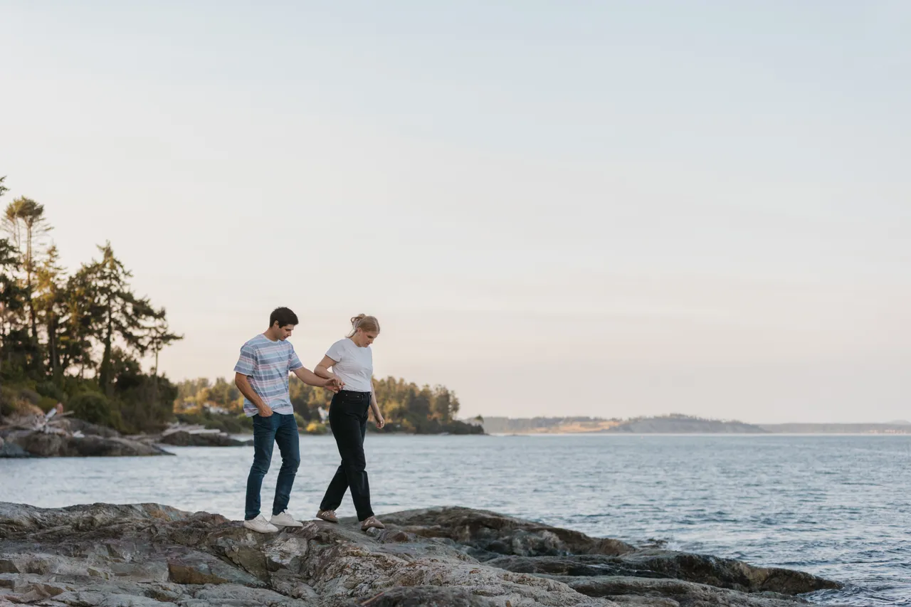 Couple walking hand in hand along rocky shoreline with large sky in background