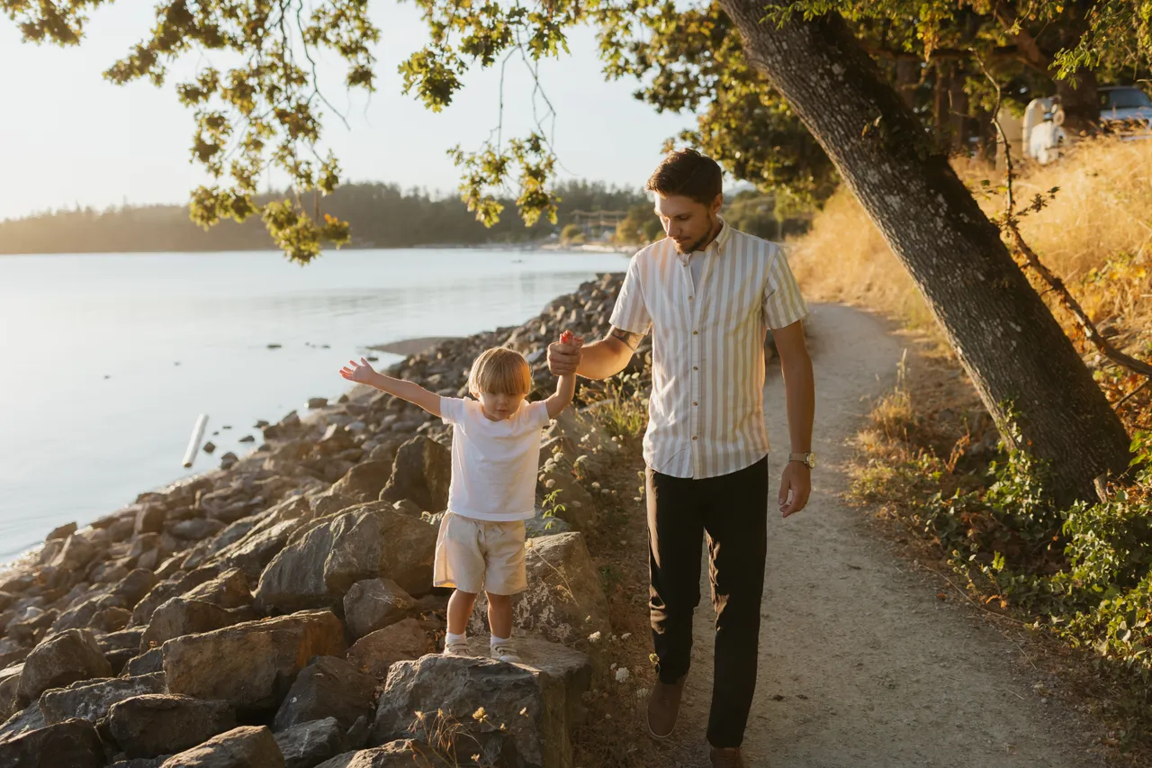 Father and child walking along a sunny shoreline path
