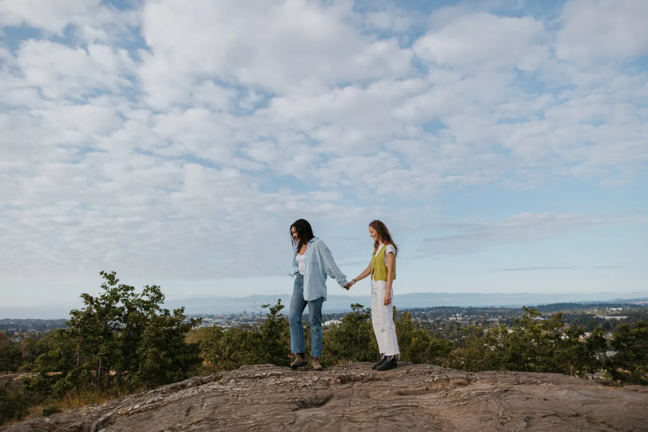 Couple holding hands on a rocky hilltop with sky in background