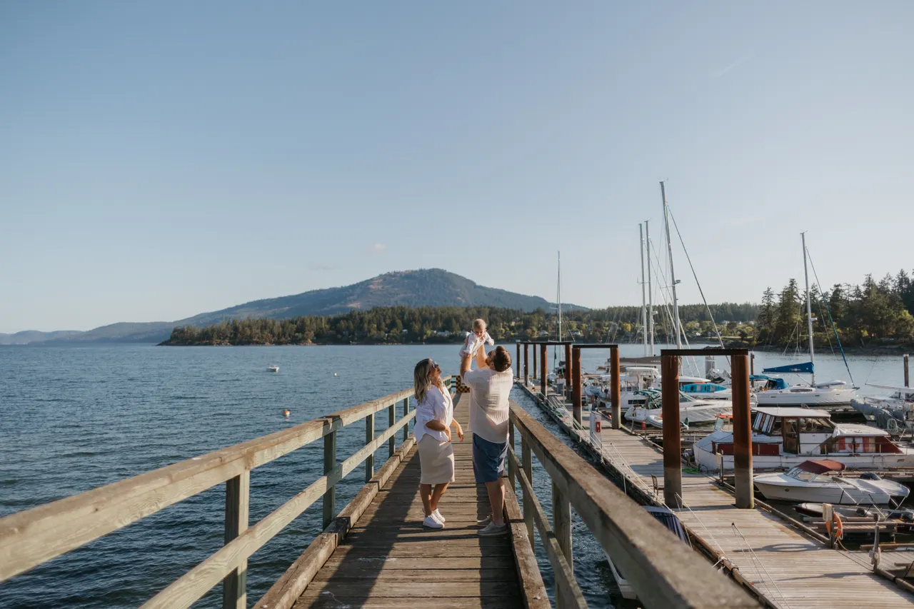 Family enjoying a sunny walk on a coastal pier near boats with mountains in background