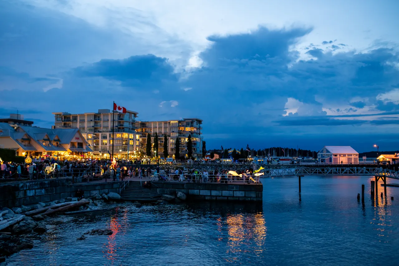 Illuminated harbour buildings and pier mirrored in calm water at blue hour