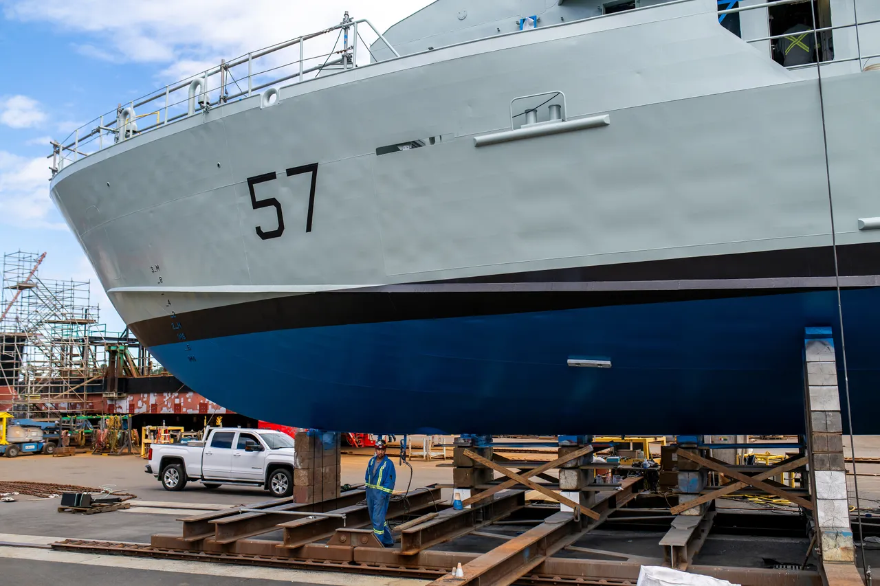 Shipyard Worker Beneath a Grey Vessel's Hull on Keel Blocks