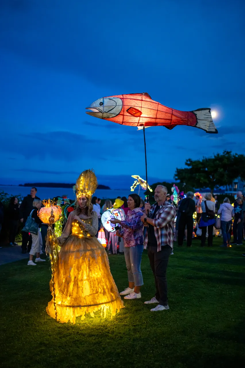 Red salmon lantern raised above a costumed performer in a glowing gown at dusk