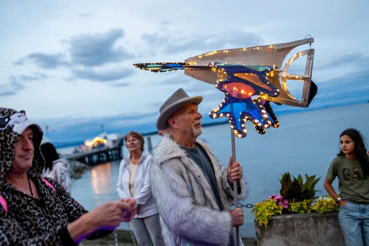 Man in Fedora Carries Illuminated Stingray Lantern at Waterfront Evening Parade