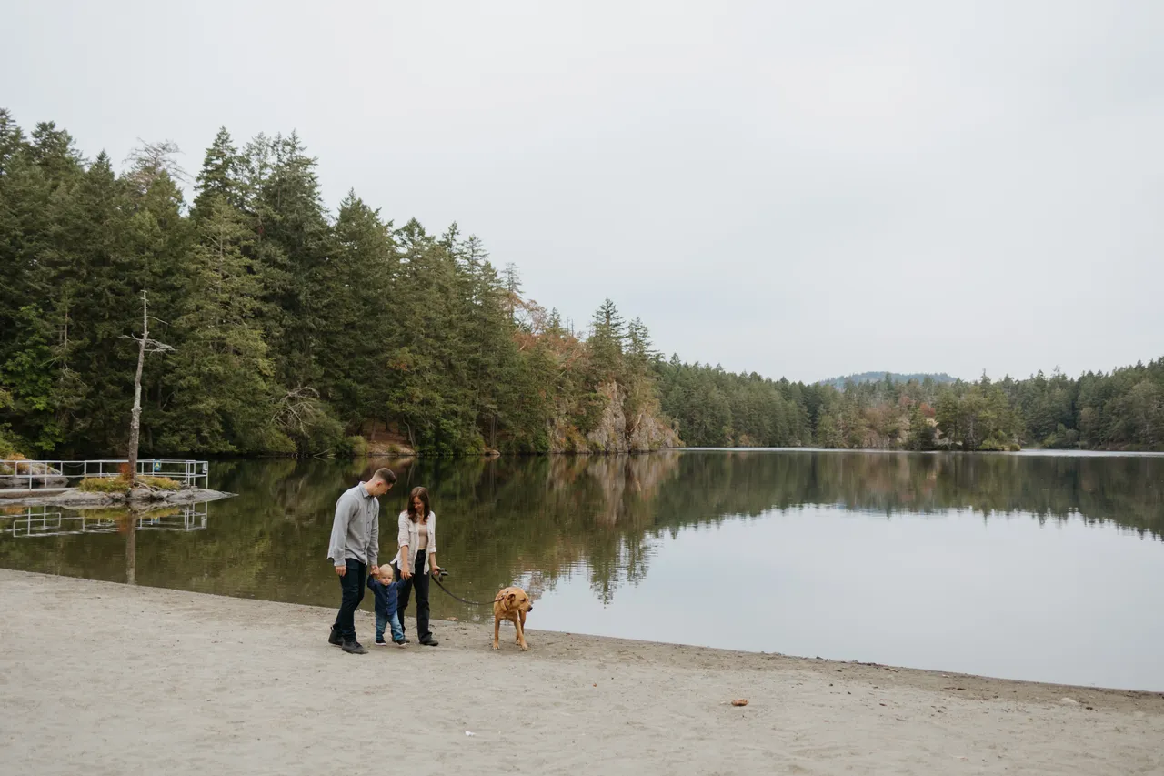 Family with dog walking along a calm lakeshore surrounded by forest