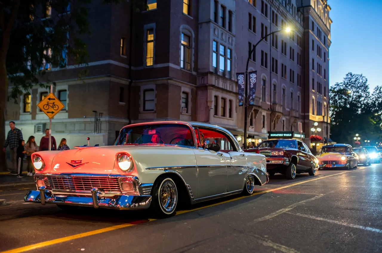 Classic 1956 Lowrider Cruising Past a Historic Hotel at Dusk
