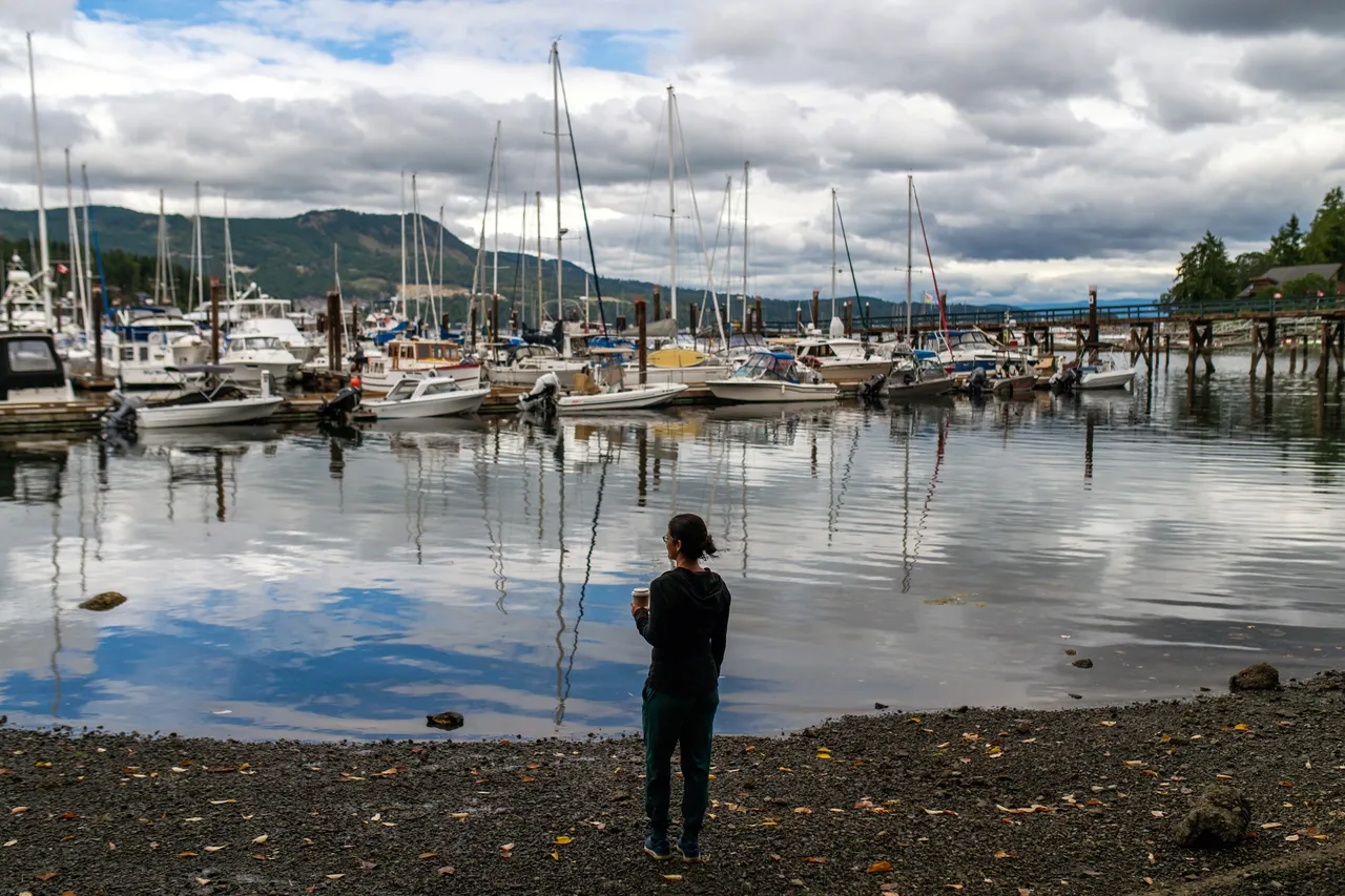 Woman standing by water with coffee - 1 - Dr. Sienna Bourdon