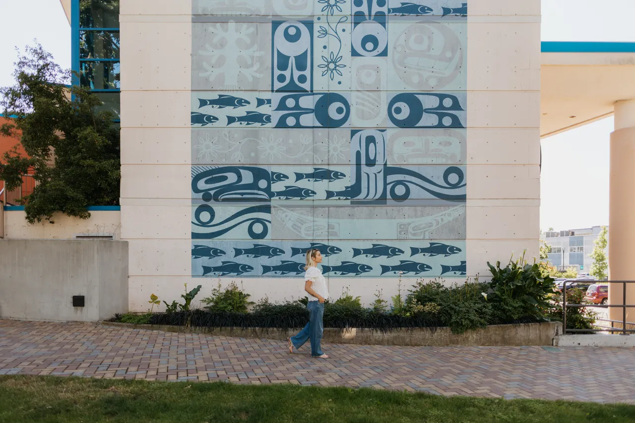 Woman Walks Past Indigenous Fish Mural During the Day