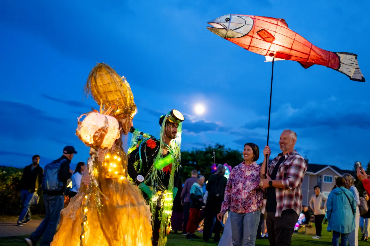 Salmon lantern held aloft over a glowing costumed figure against a deep blue sky