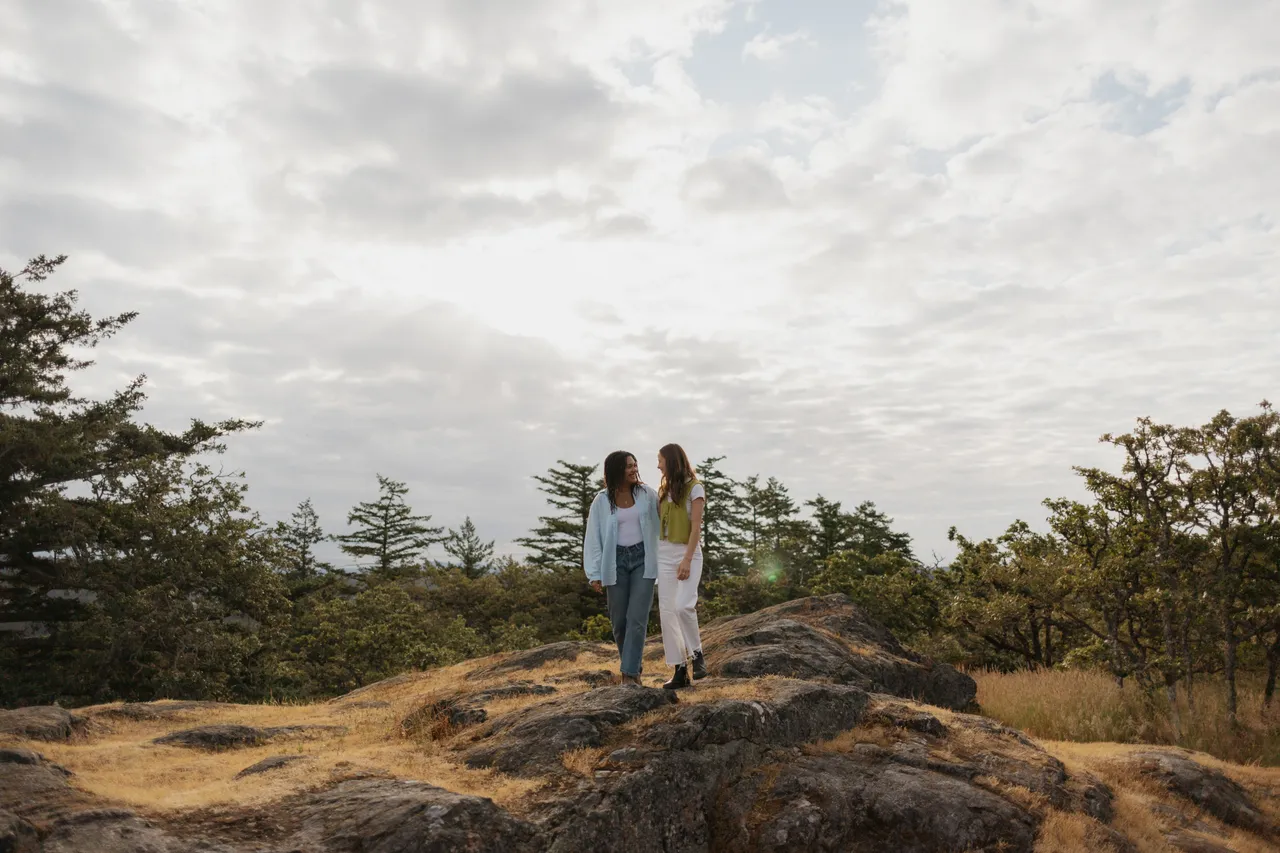 Couple walking on rocky hill under cloudy sky with trees in background