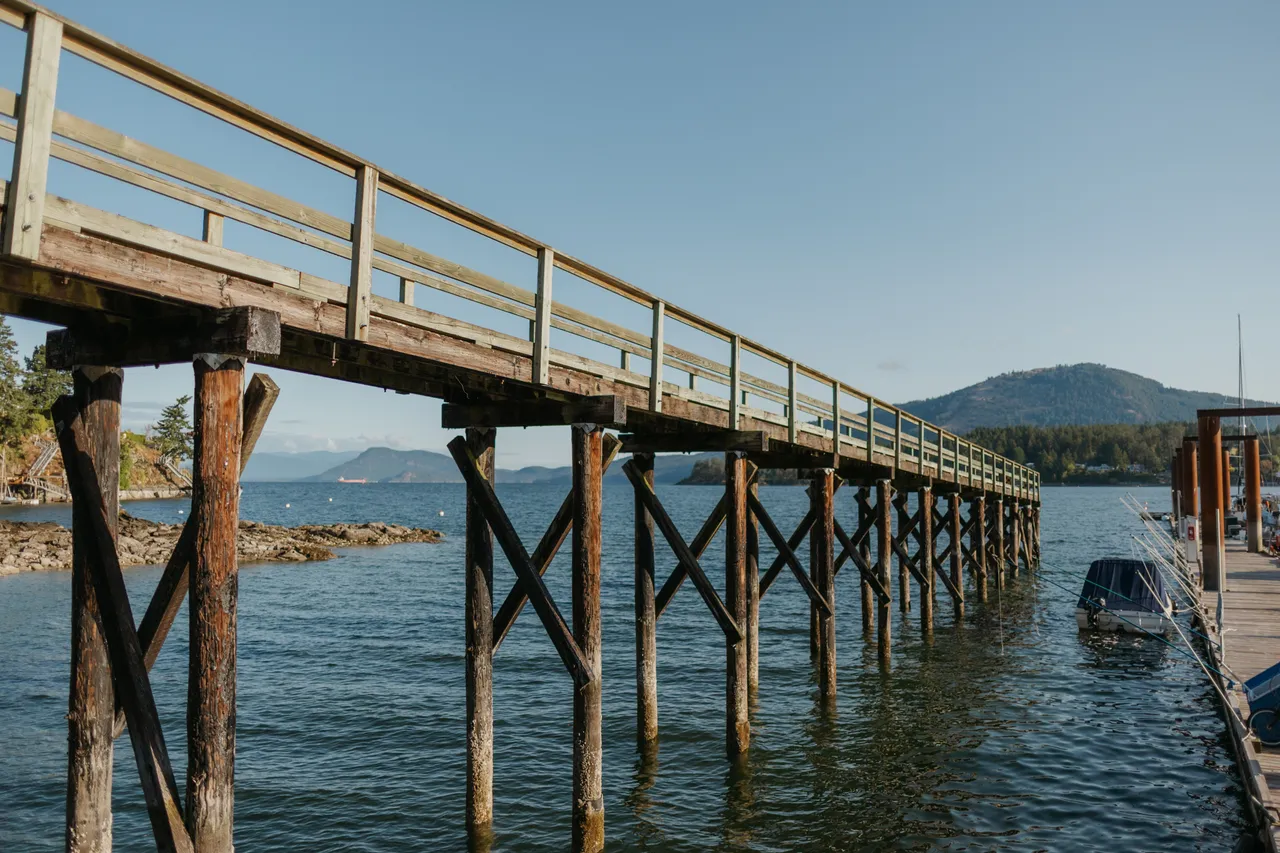 Wooden pier stretching over calm coastal waters at sunrise with mountains in background