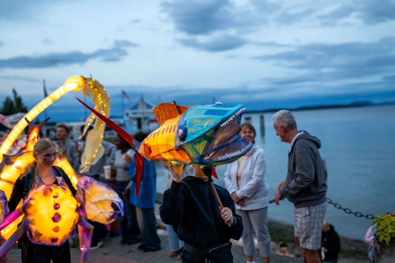Child Carries Handmade Fish Lantern on Pole at Waterfront Evening Parade