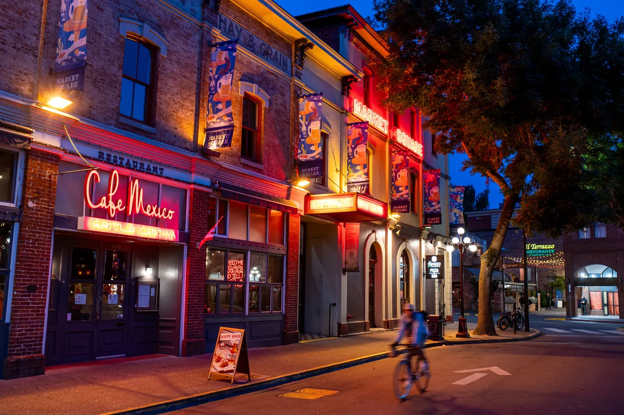 Cyclist Passing Neon-Lit Market Square in Old Town Victoria