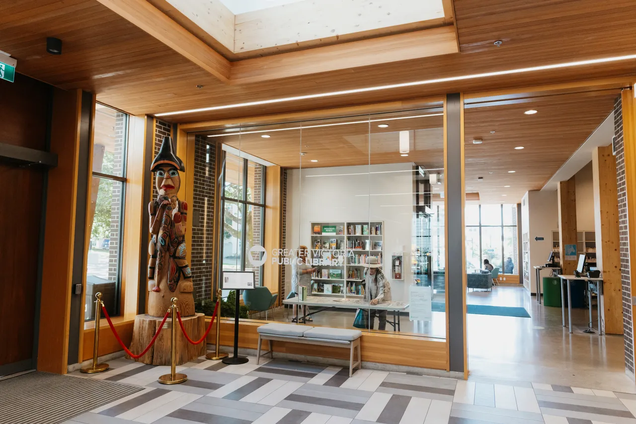 A spacious, modern lobby with wooden beams, glass walls, and a carved totem pole statue.
