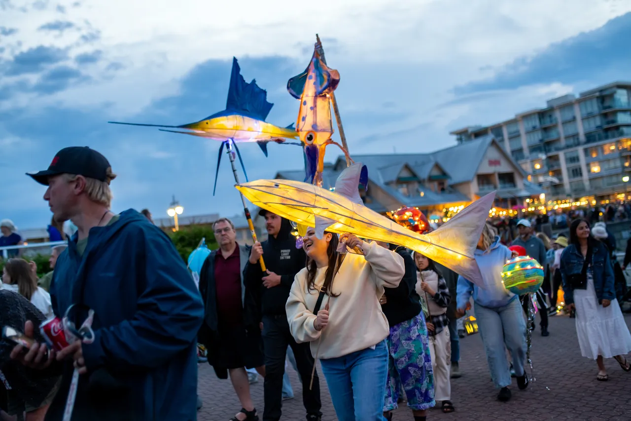 Spectators watch golden marlin lanterns pass by on a waterfront promenade