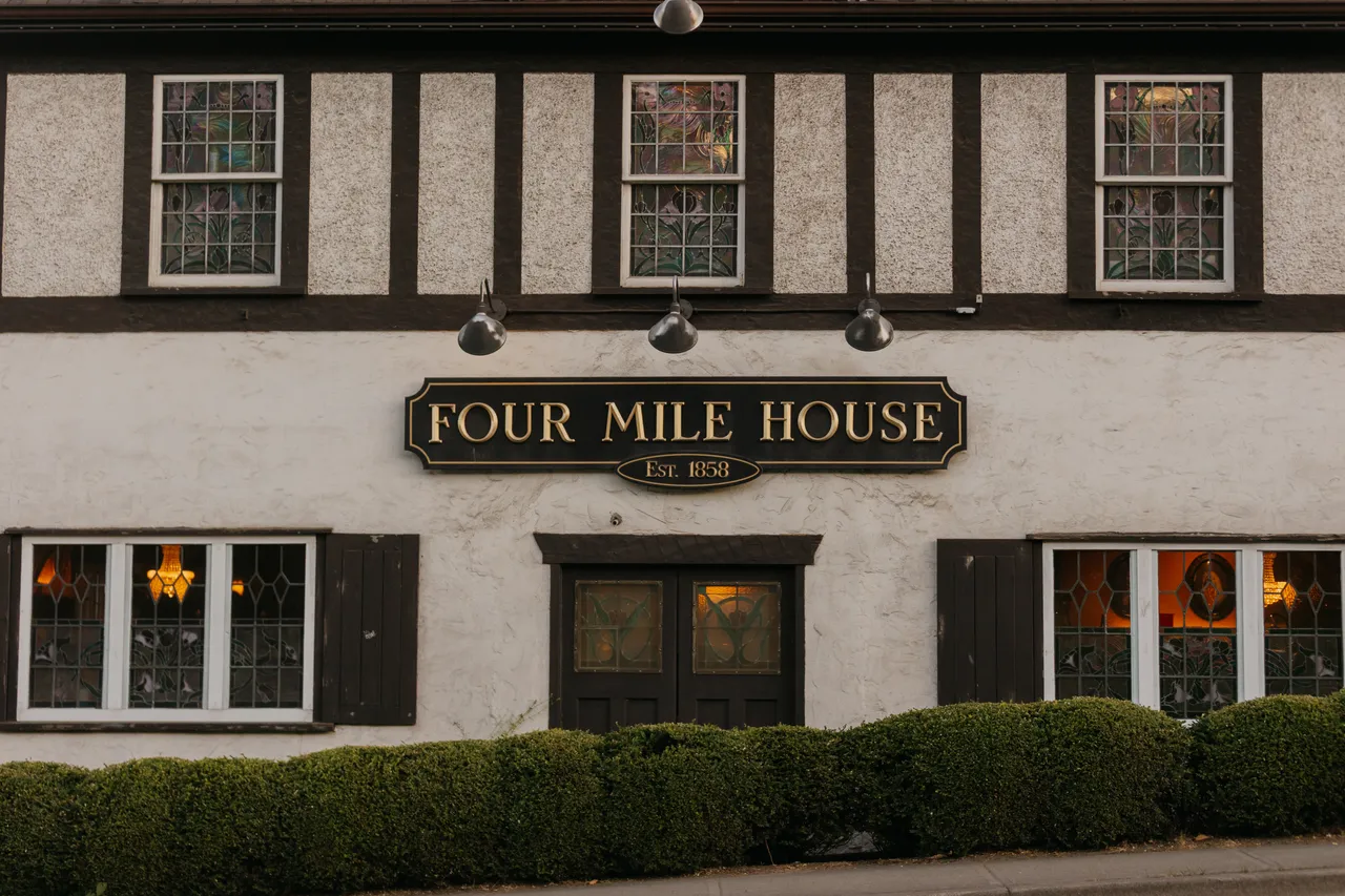 Charming heritage pub with warm evening lights aglow behind bushes