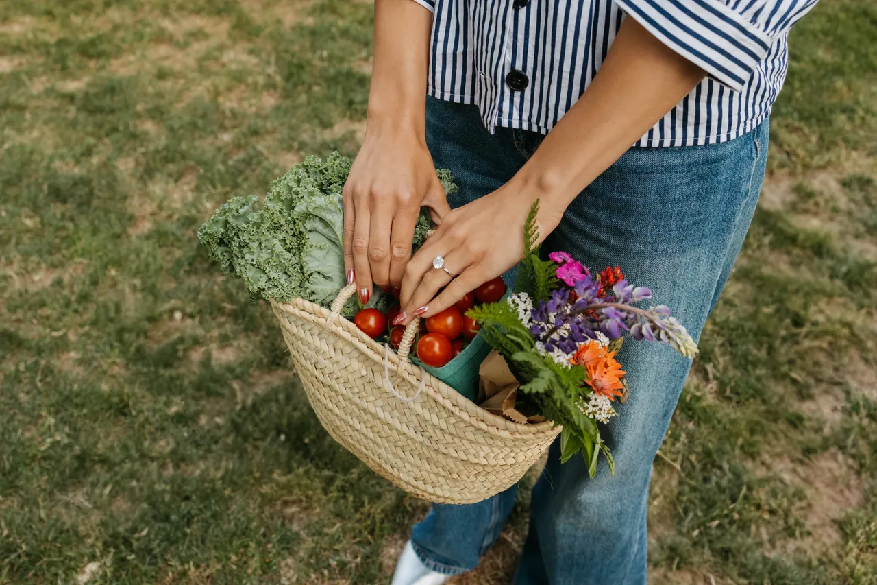 Person holding a basket of fresh vegetables and flowers