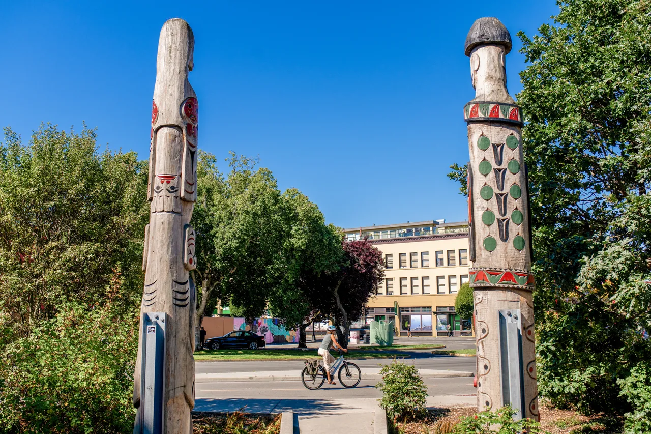 Woman cycling by totems - 1- Victoria